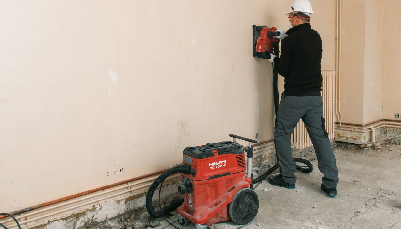Un operatore realizza dei tagli su muro interno con una scanalatrice DCH 150 e un aspirapolvere da cantiere